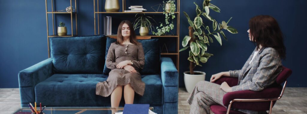 A woman sits on a couch with her eyes closed as her therapist speaks to her calmly