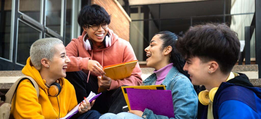 A group of teenagers sit on school steps talking and laughing