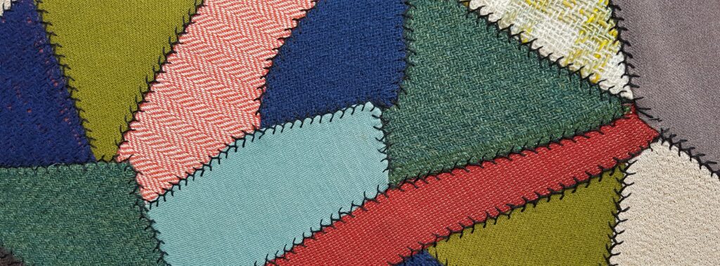 Close up view of different colored patches of cloth stitched together to form a quilt