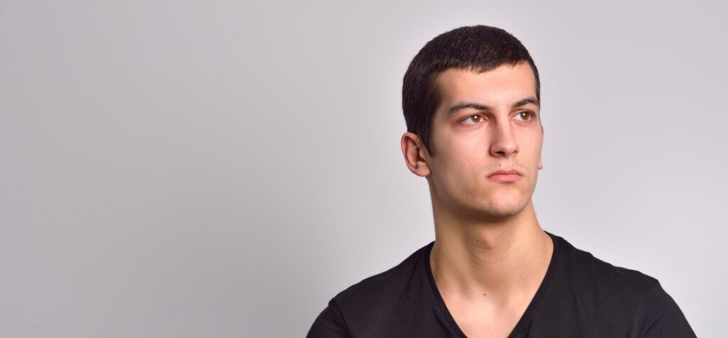 A man stares thoughtfully into the distance with a gray background behind him