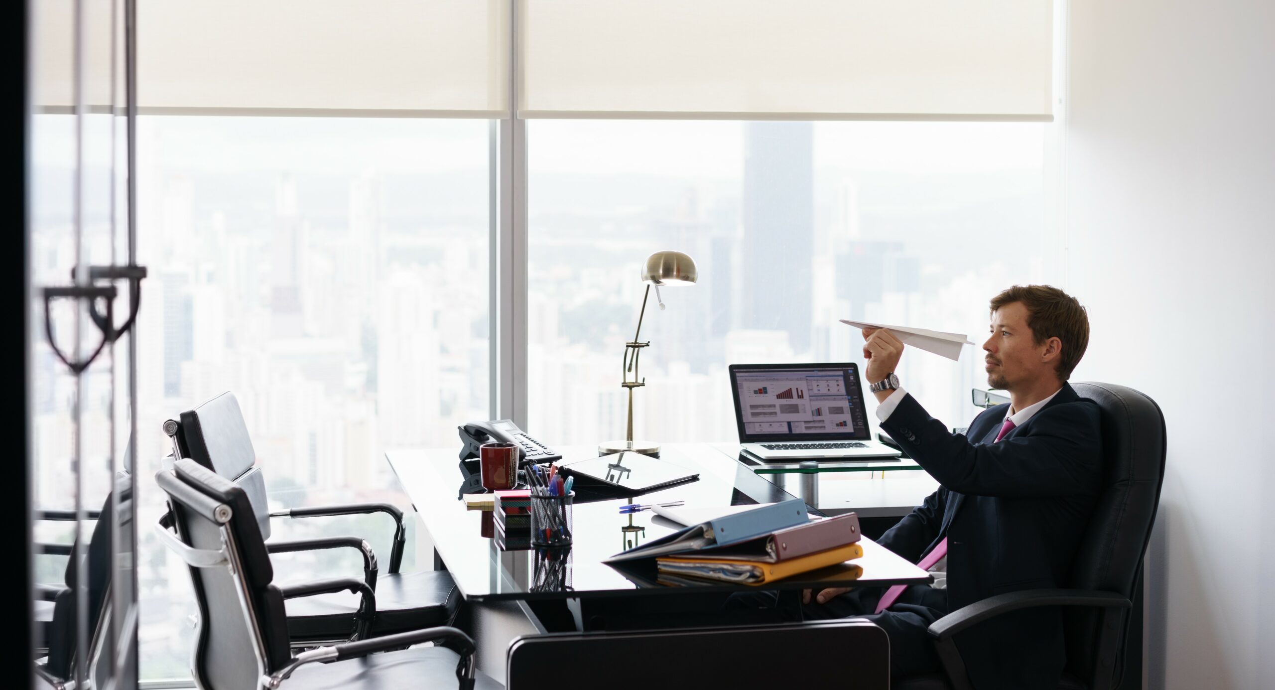 A man sits at his desk ignoring the computer and playing with a paper airplane