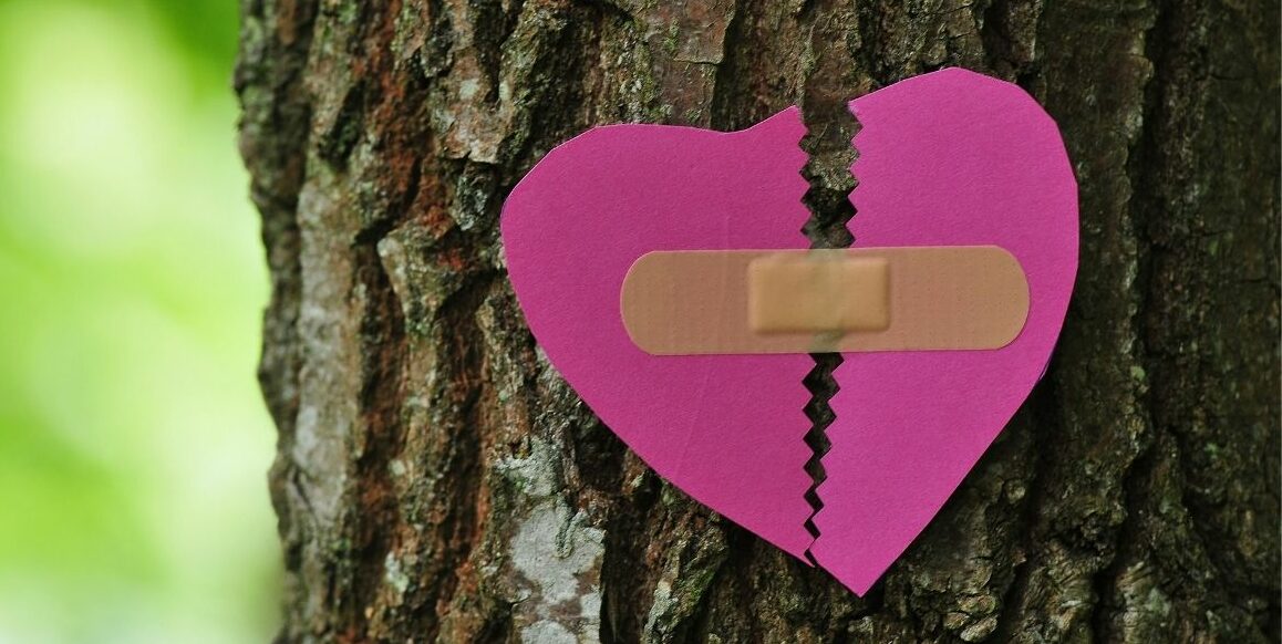 A paper heart ripped and put back together with a bandaid.