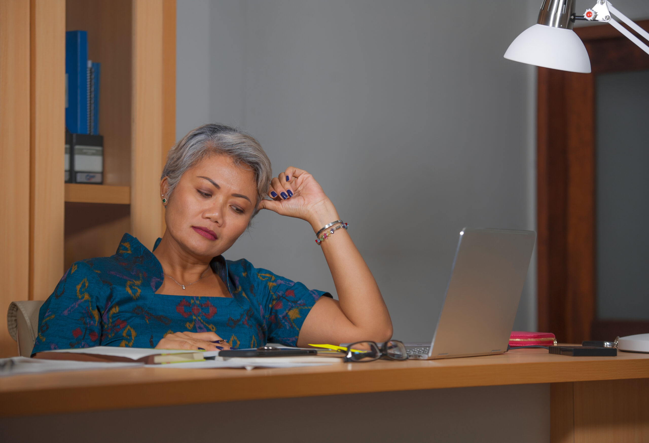 A woman sitting at a desk looks downward thoughtfully