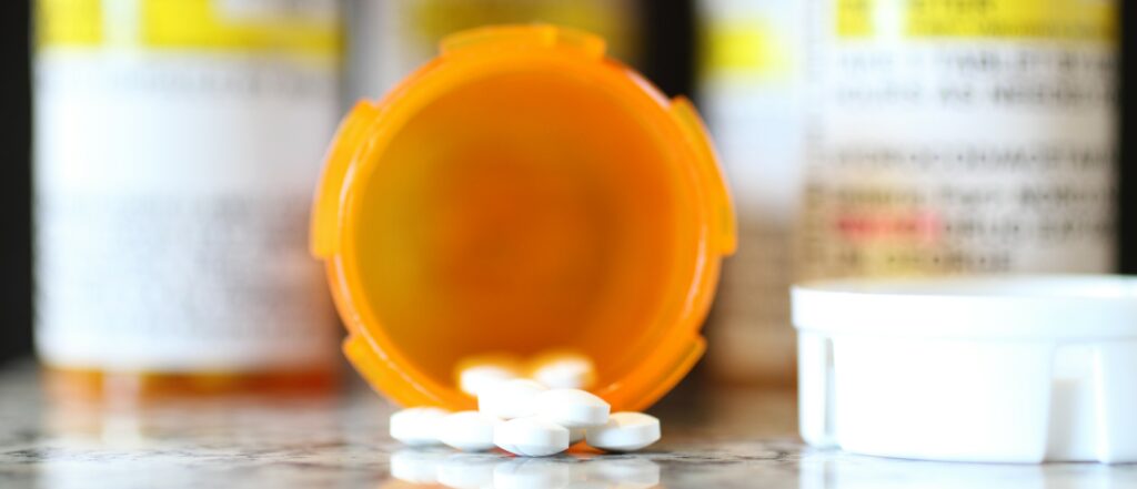 An open yellow bottle lays on is side with white pills spilling out of it