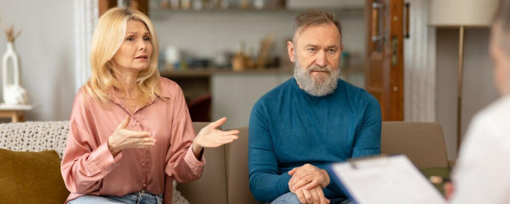 An unhappy middle aged couple sits on a couch talking to their therapist