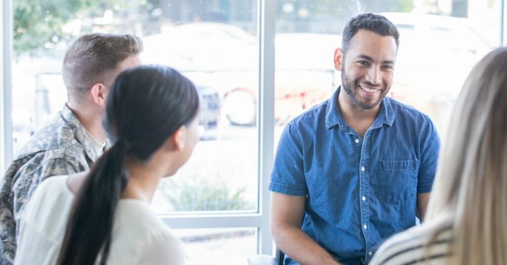 A man smiling in a group therapy session.