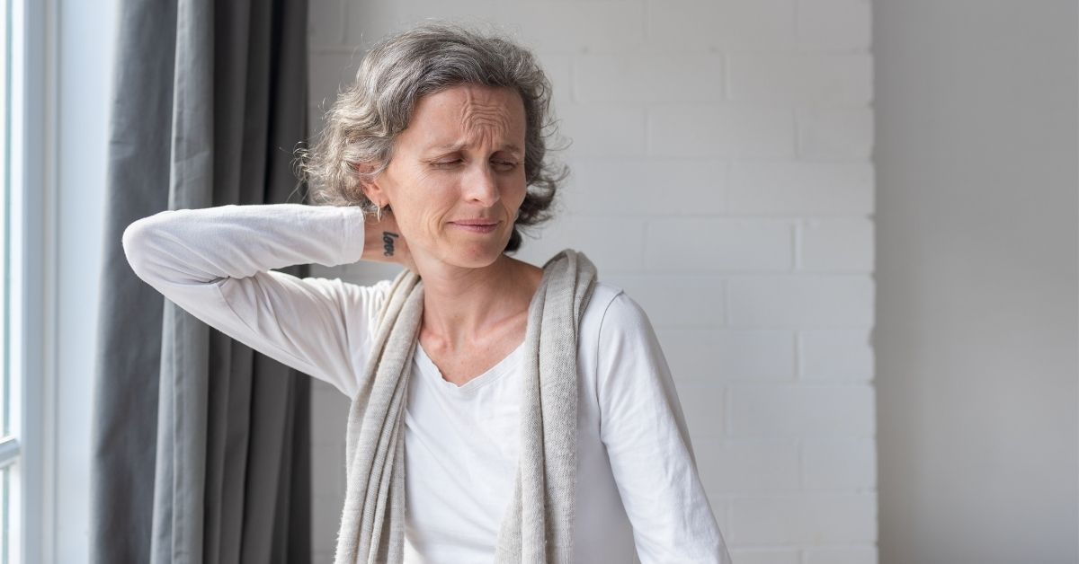 A senior woman rubbing her neck and grimacing in pain.