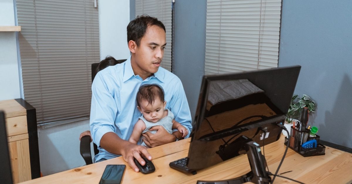 A man working from home while holding a baby.