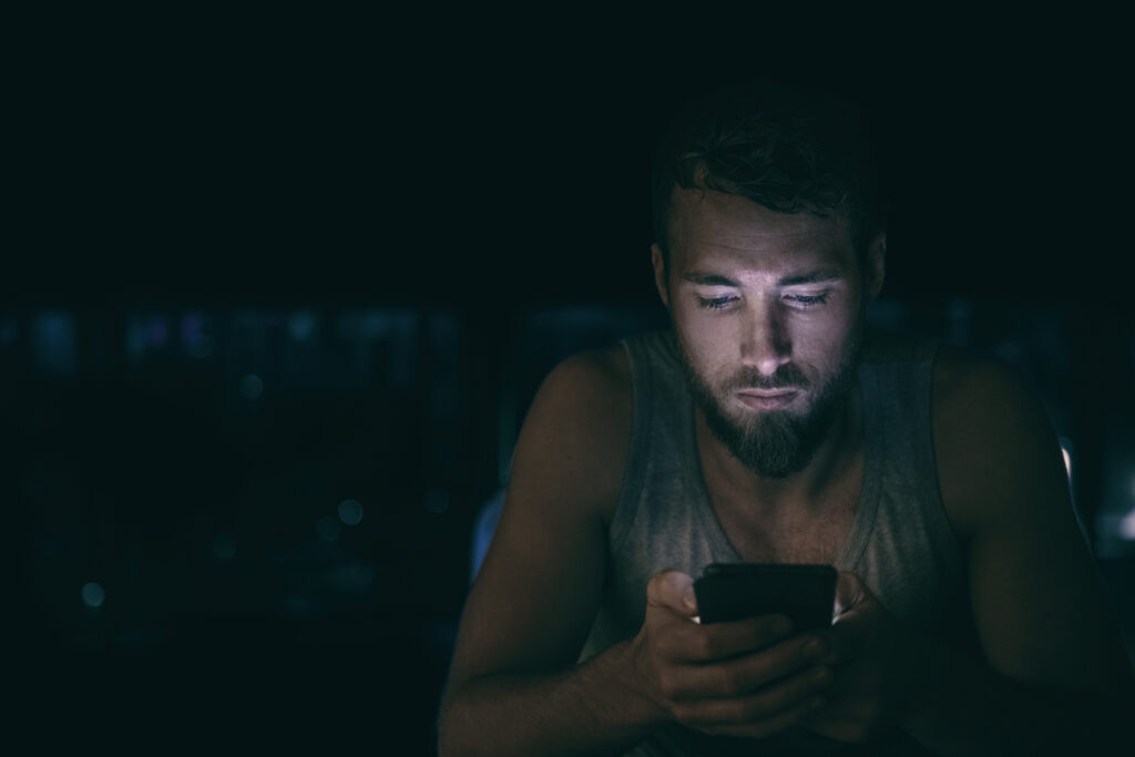 Man with beard looks at his phone late at night