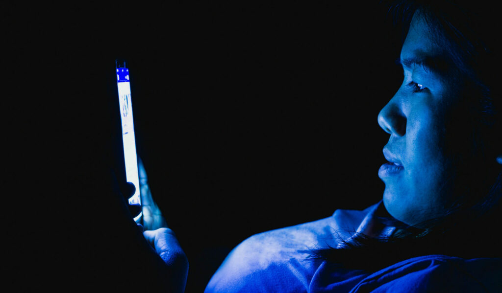 Asian American woman staring at cell phone in the dark