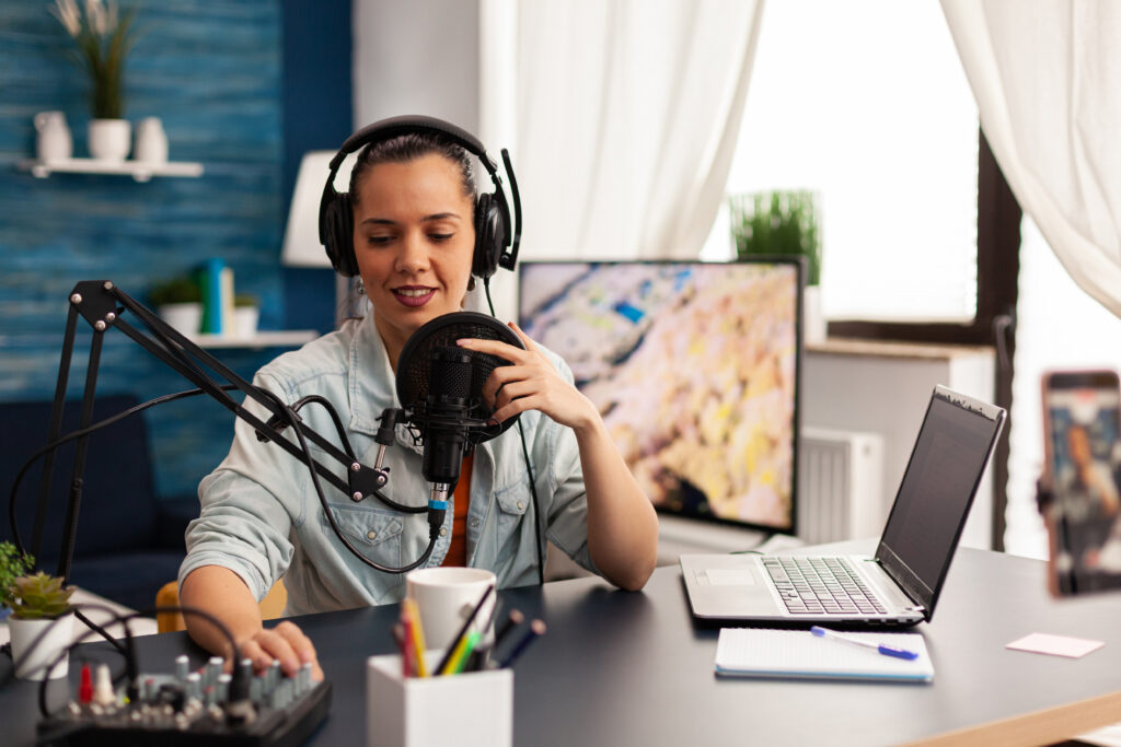 Female podcaster sits in front of a laptop adjusting settings on a soundboard