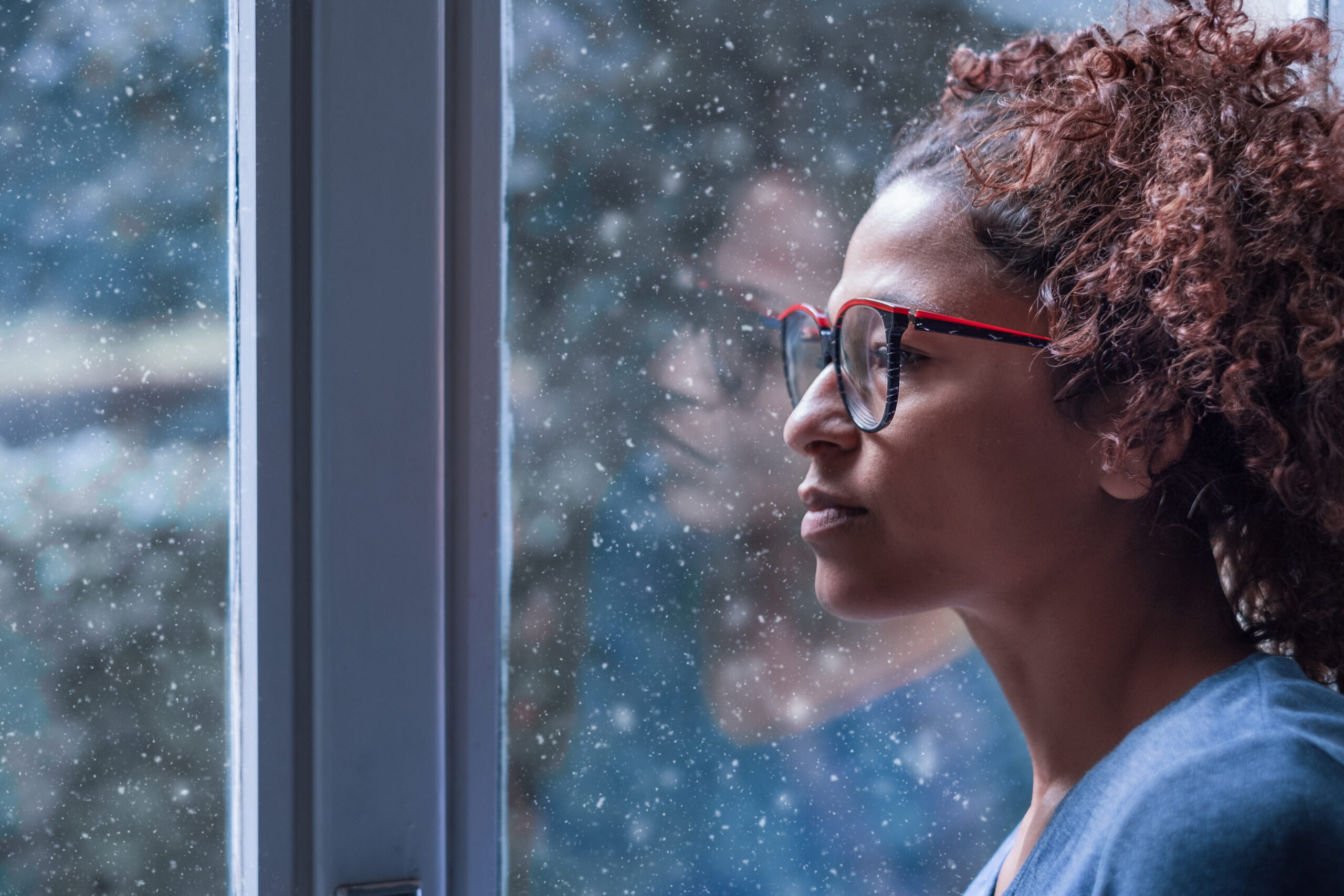 A woman stares out of a woman thoughtfully while snow falls