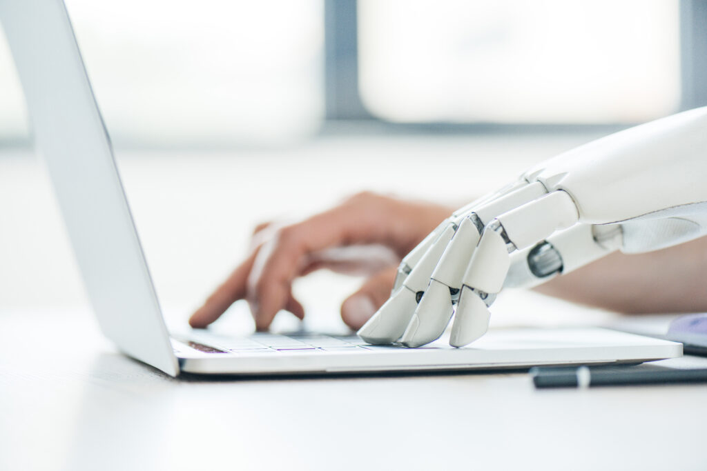 Image of a pair of hands typing on a keyboard, one is human and one is robotic