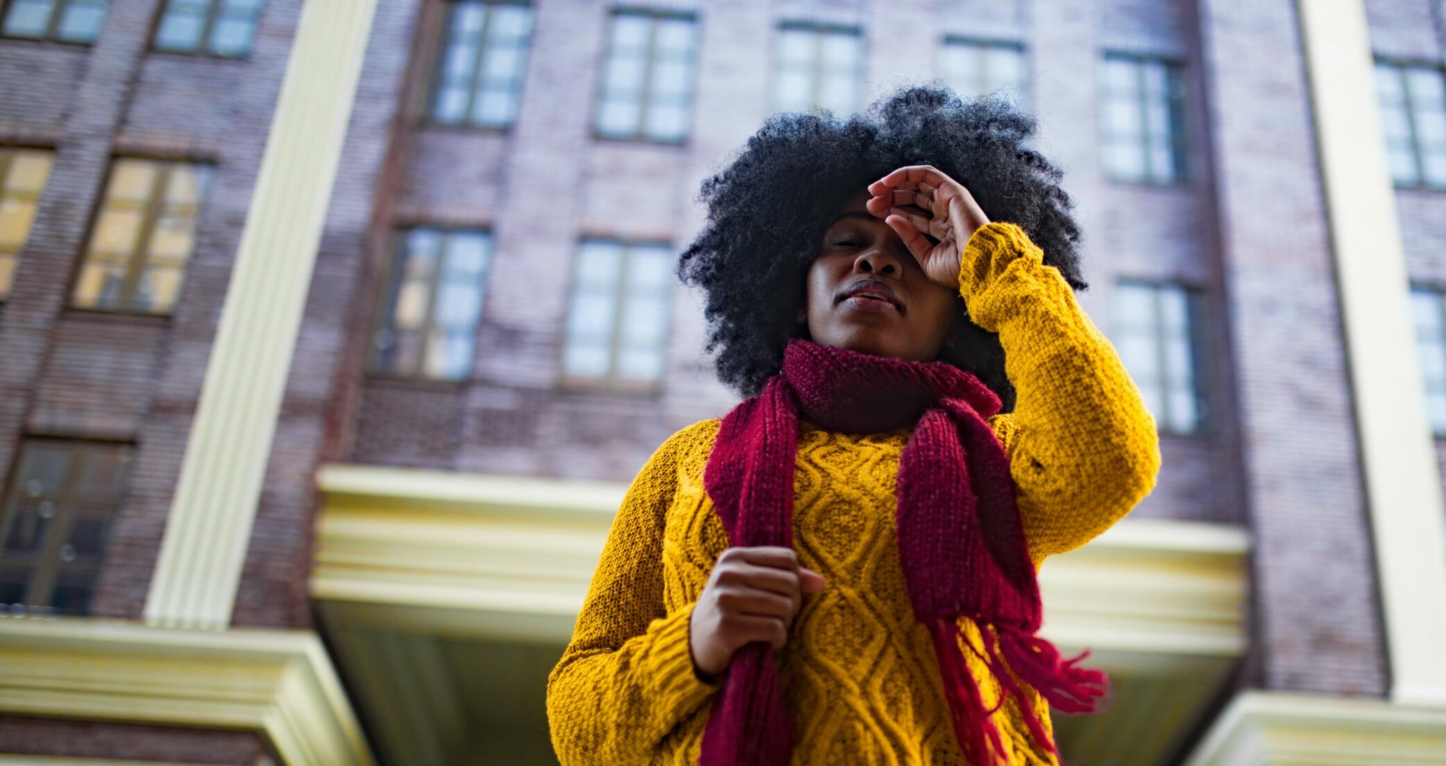 A woman touches her forehead deep in thought outside of a tall building