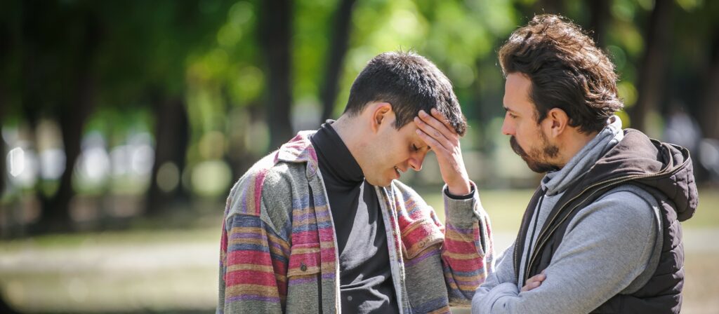 Two men stand outside looking serious as they discuss their relationship