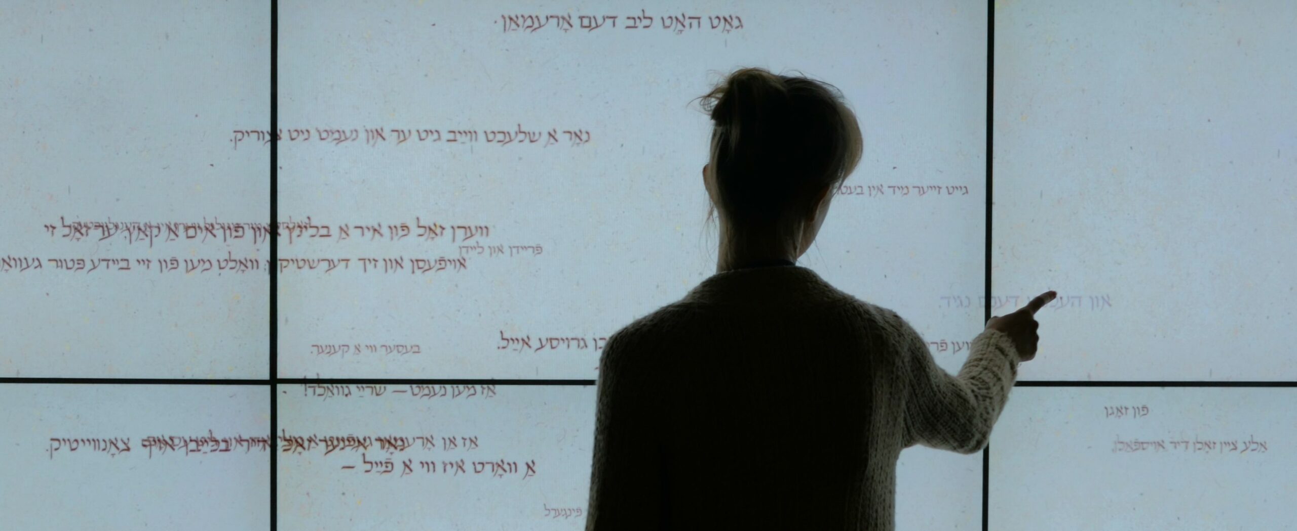 A woman uses a touchscreen displaying Hebrew phrases at a history museum