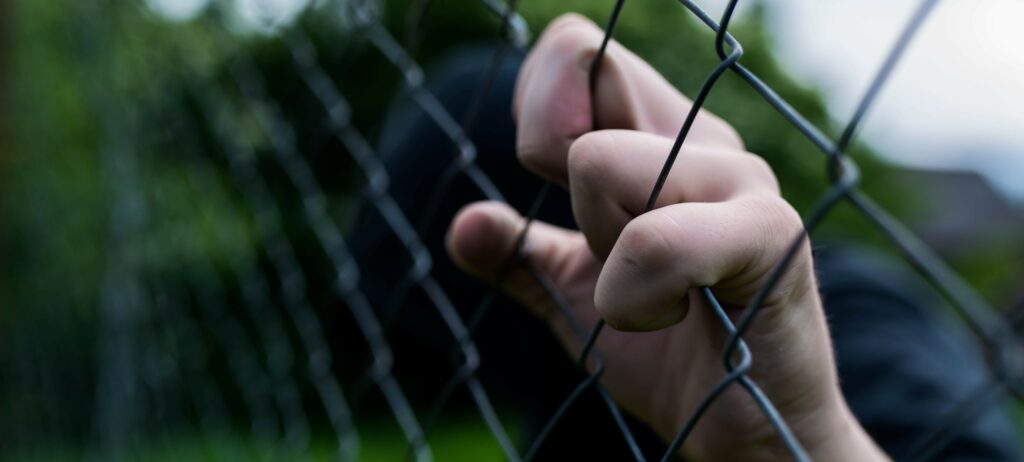 Close up image of a hand gripping a chain link fence