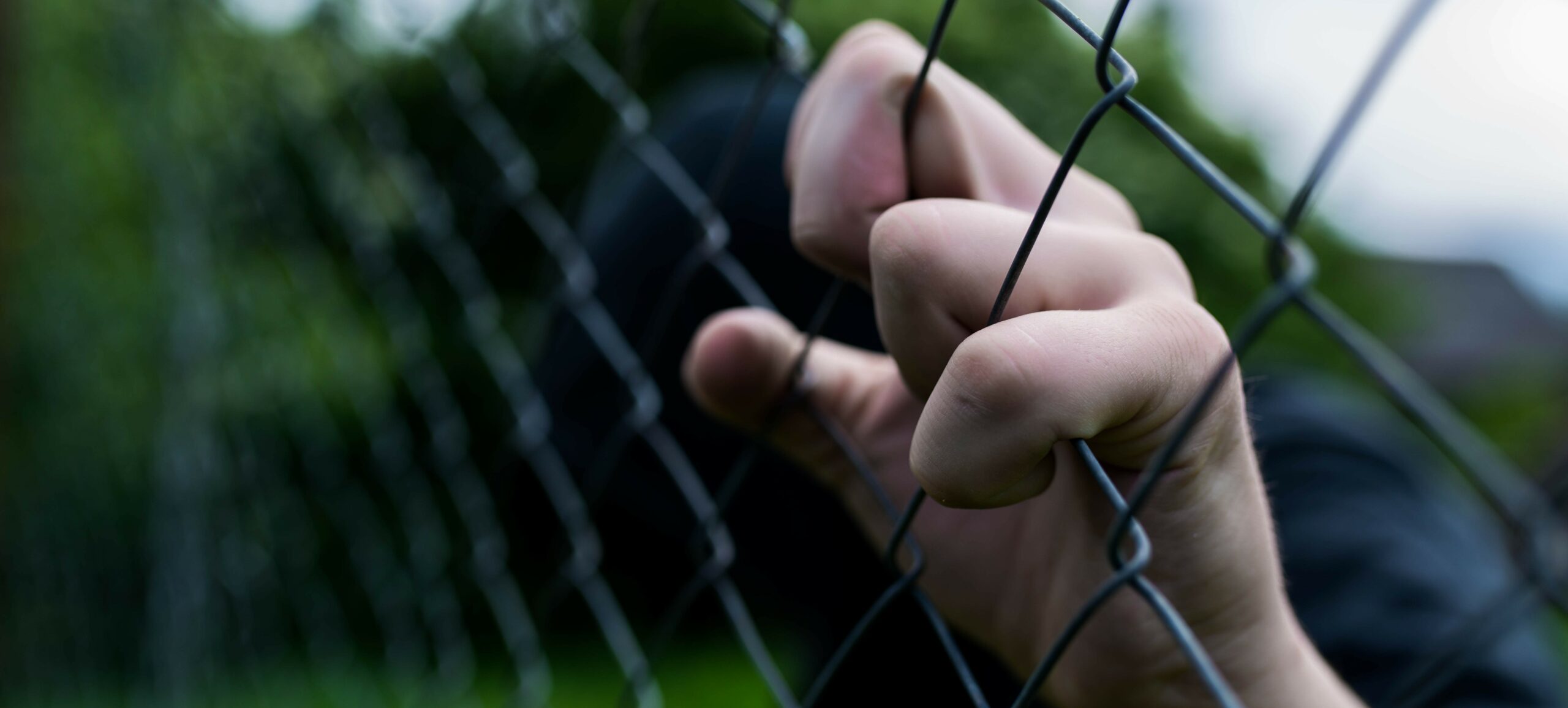 Close up image of a hand gripping a chain link fence
