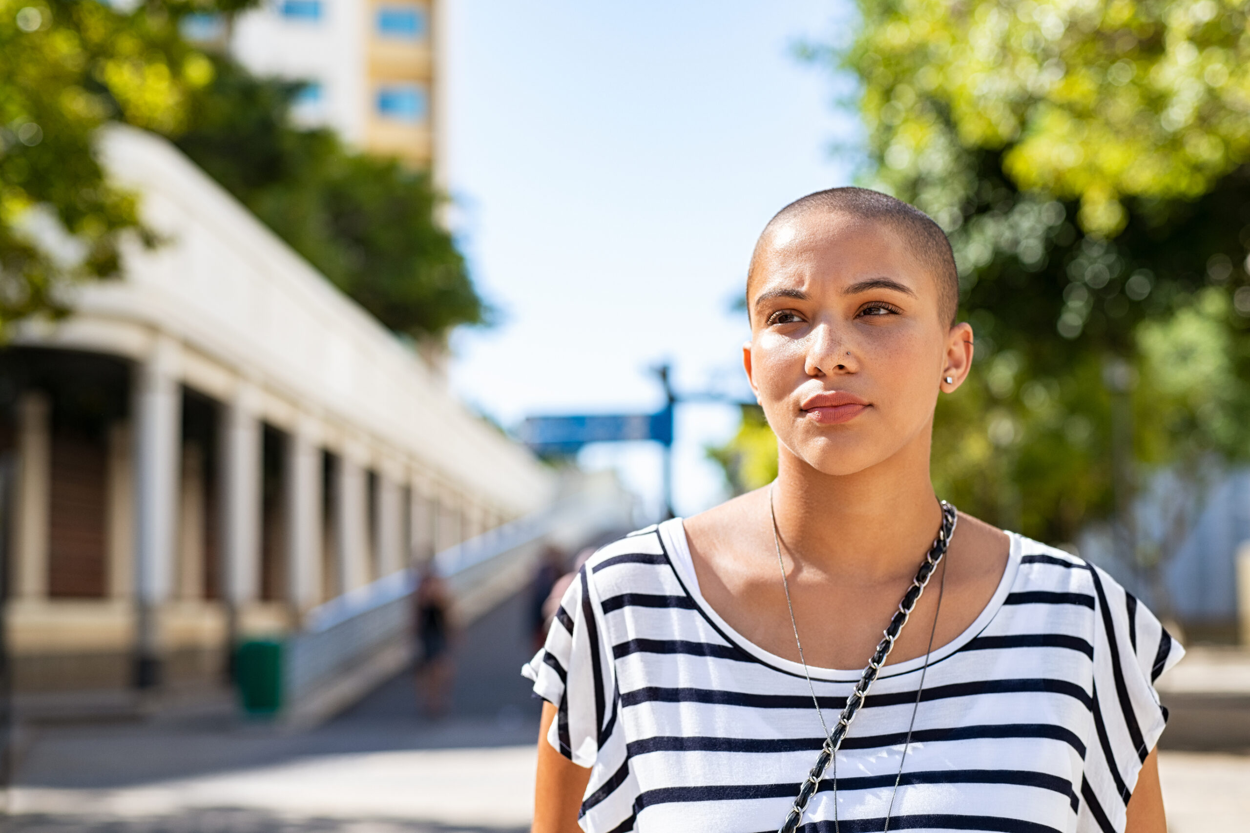 Young woman with a shaved head and a striped shirt stands outside