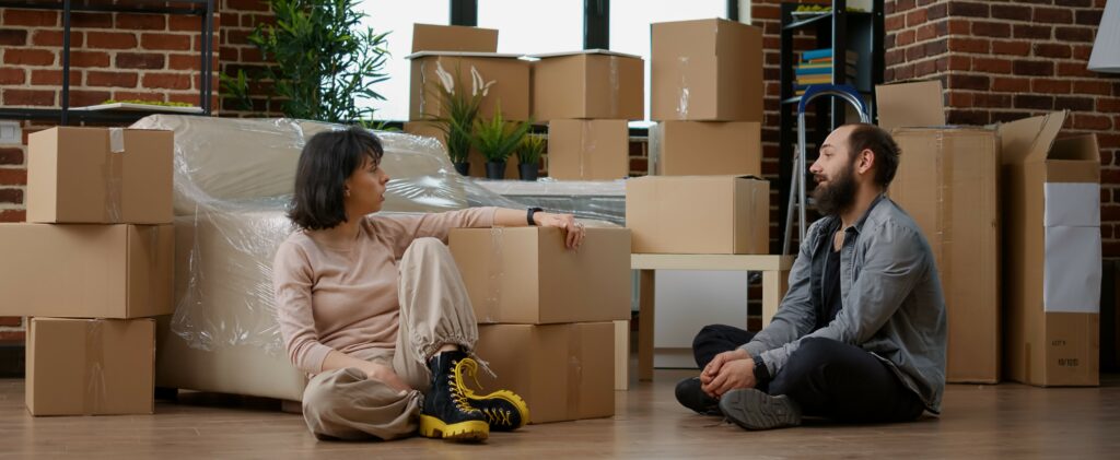 A couple sits on the ground surrounded by packed boxes having a disagreement