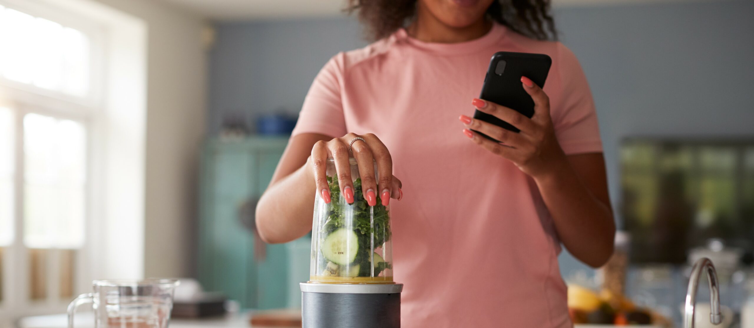 A woman makes a smoothie while typing on her phone