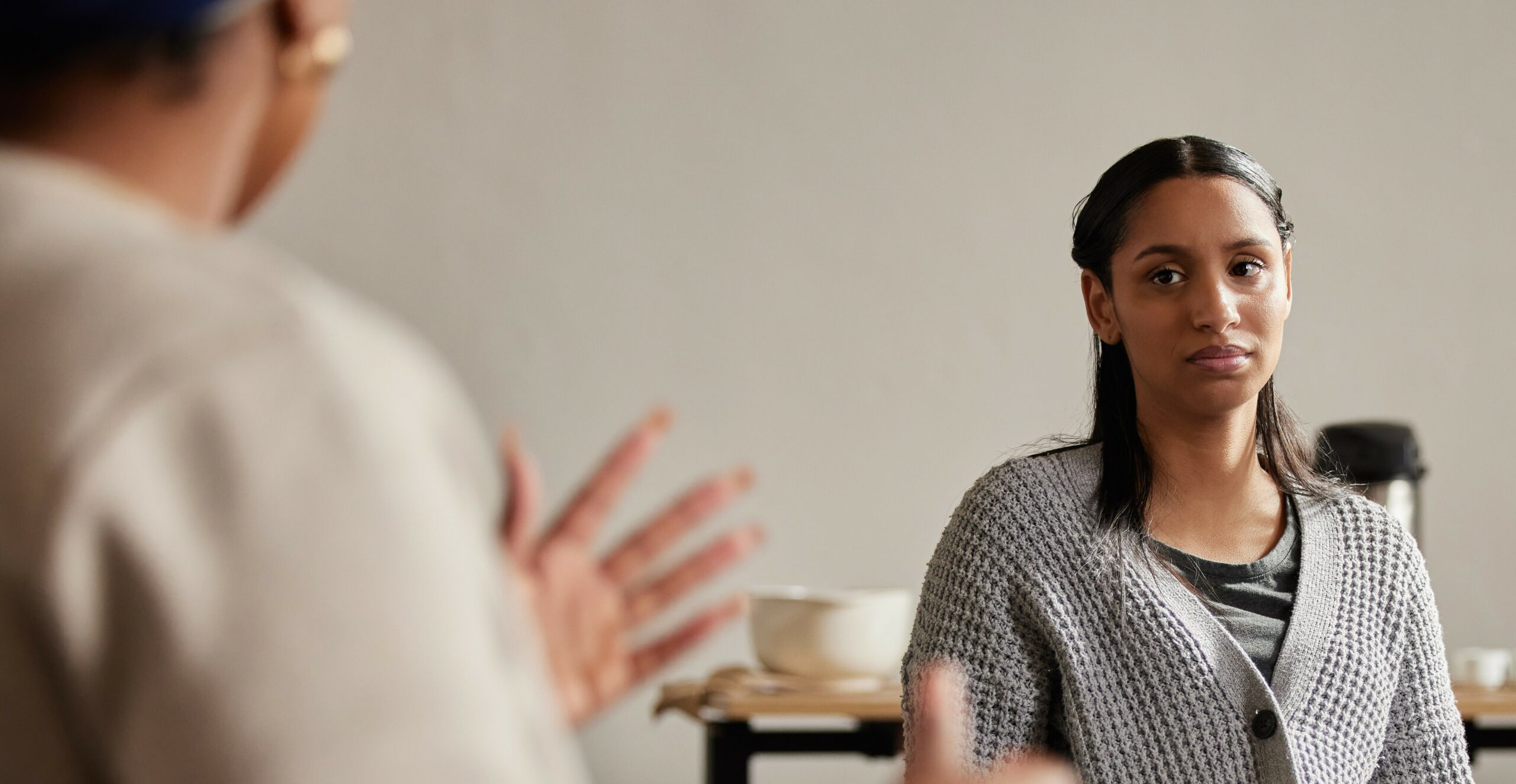 A Black woman sits in a therapy session looking at the person speaking with a difficult to read expression