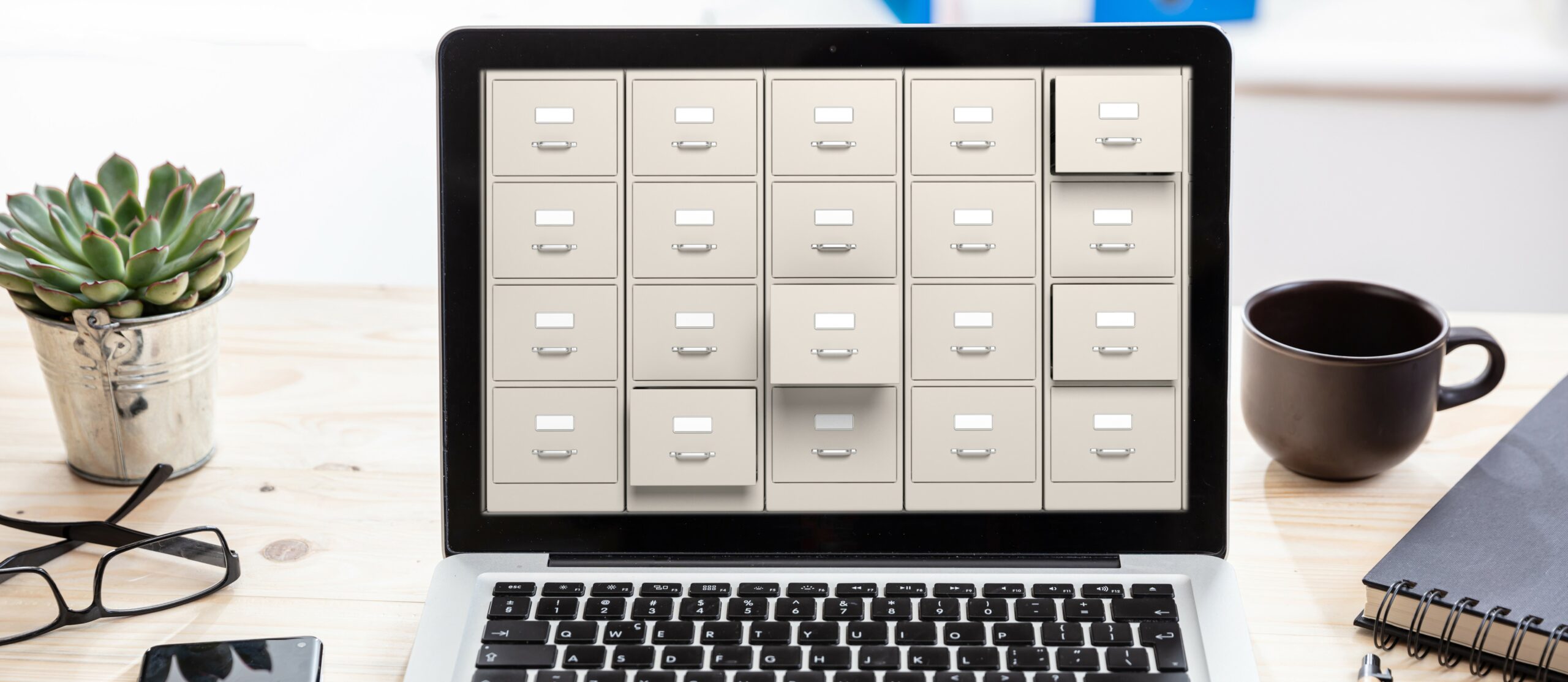 A laptop sits open on a desk displaying a wall of filing cabinets