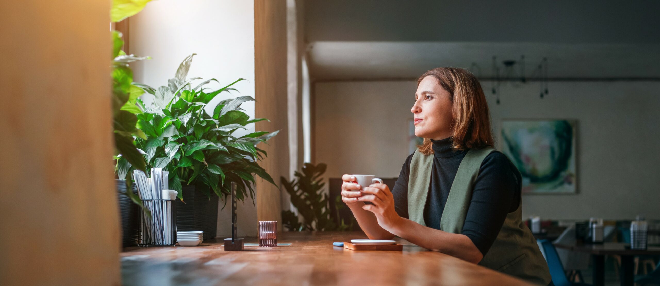 A middle aged woman sits in a cafe looking out a window thoughtfully